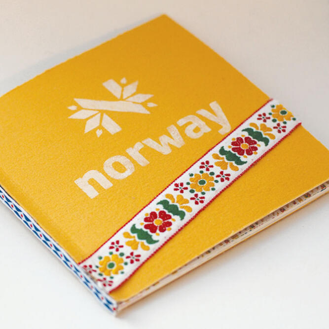 yellow square book with "N" snowflake logo and "norway" and a ribbon