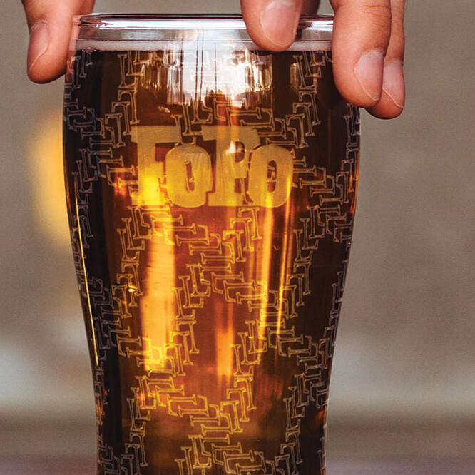 pint glass with fingers on top, etched with "FoPo" logo and letter repeating pattern