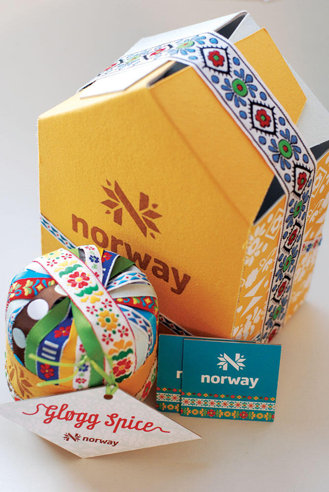 yellow box with angled top like a roof, closed with a ribbon, printed with "N" norway logo, "Glogg Spice" ribbon box in front