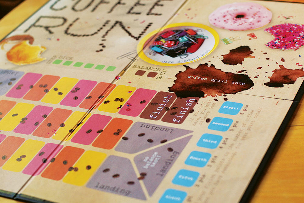 close up of board game board with pink/orange/yellow boxes and coffee spills, sprinkles, doughnuts
