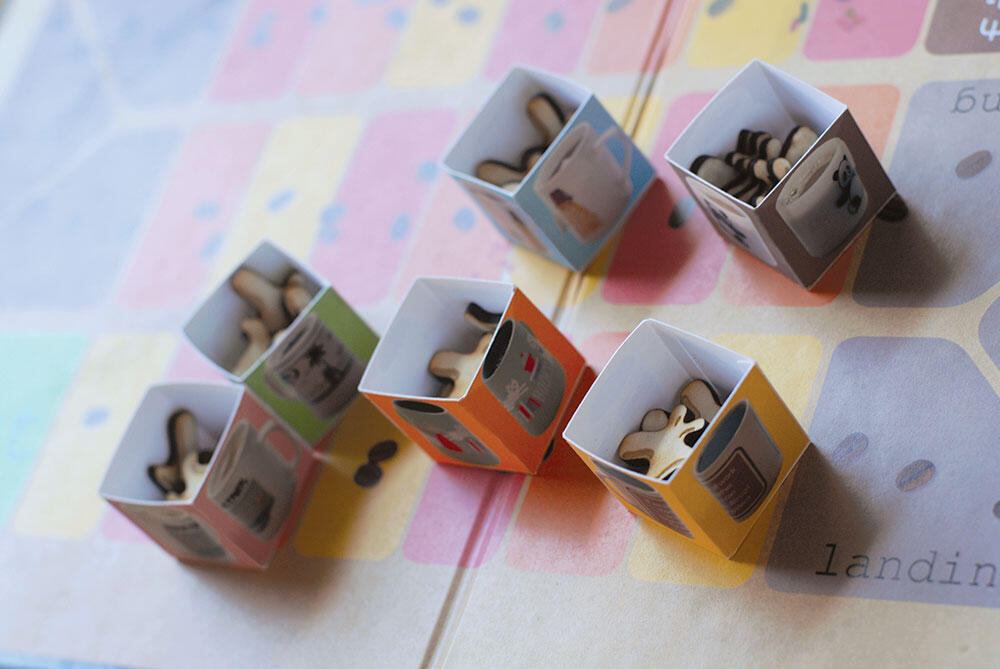small boxes with photos of mugs with small wood game pieces inside, on board